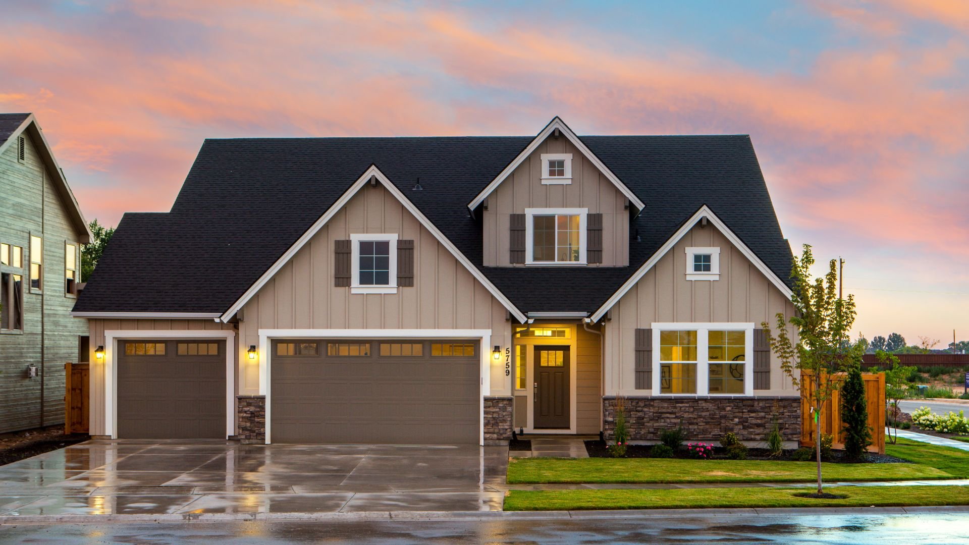 Modern suburban house with stone accents at sunset, wet driveway reflecting light