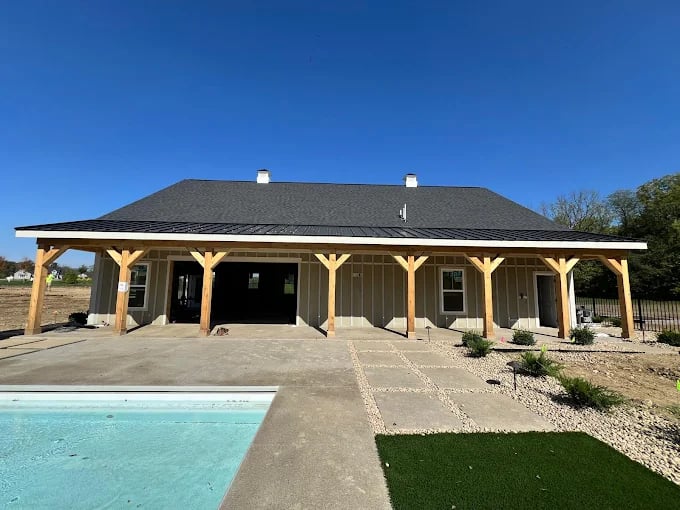 Modern barn-style building with wooden posts and swimming pool on sunny day