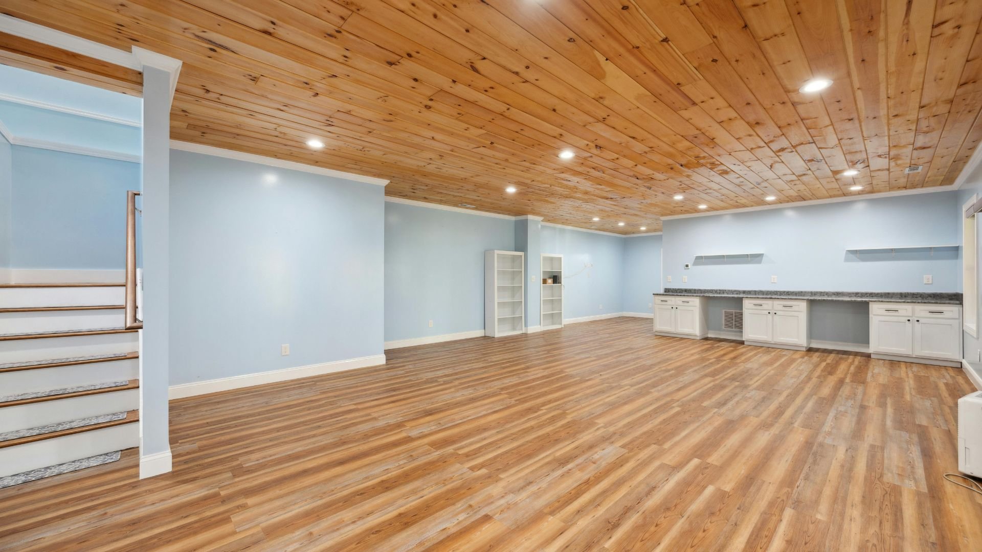 Spacious empty room with wooden floor, blue walls, and recessed lighting